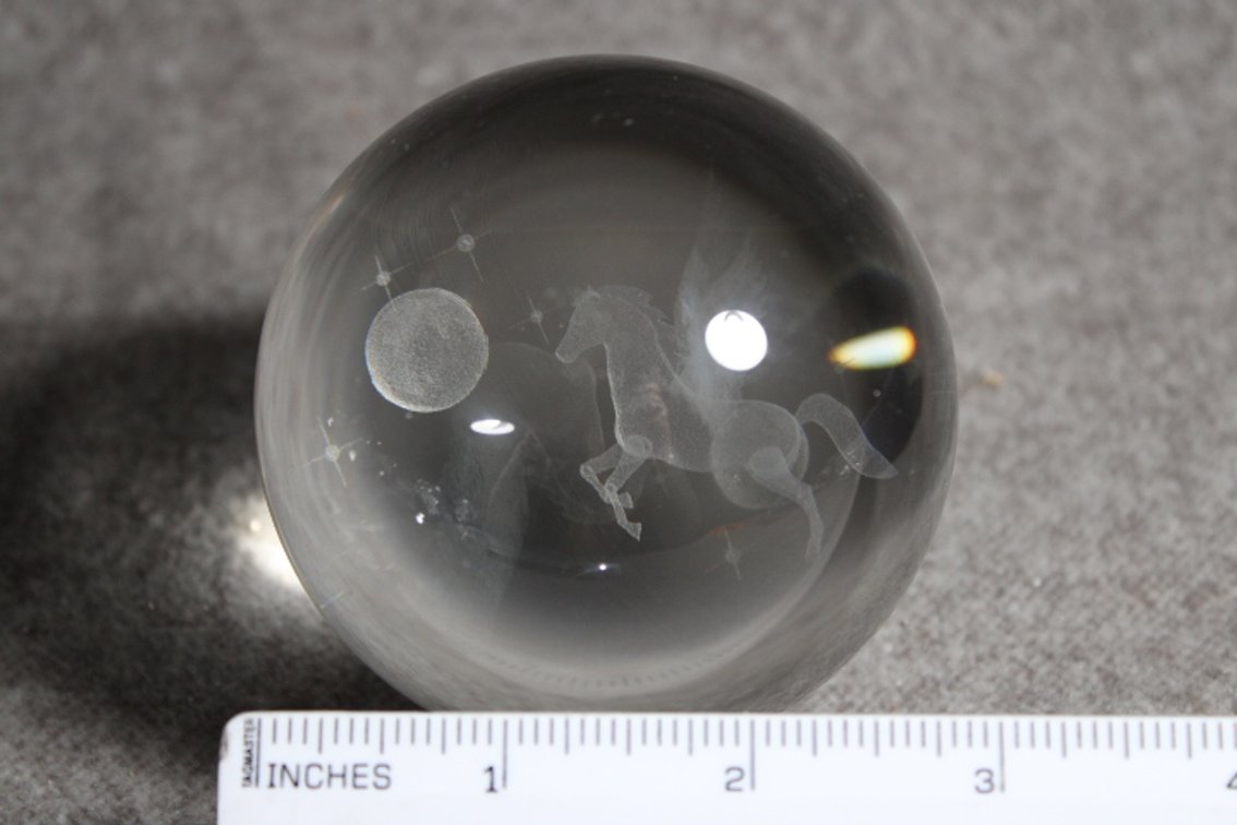 A glass sphere with a lasered image of Pegasus, sphere shown on a light box which is not included