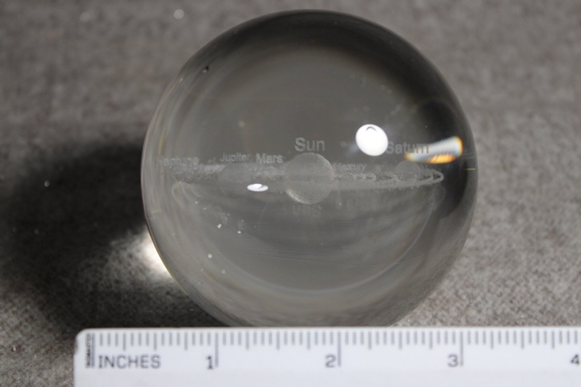 A glass sphere with a lasered image of the Solar System, sphere shown on a light box which in not included