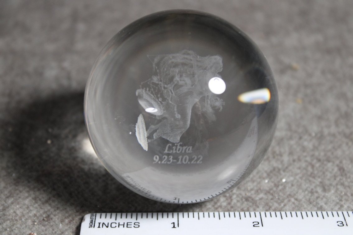 A glass sphere with a lasered image of the Zodiac sign Libra, sphere shown on light box which is not included