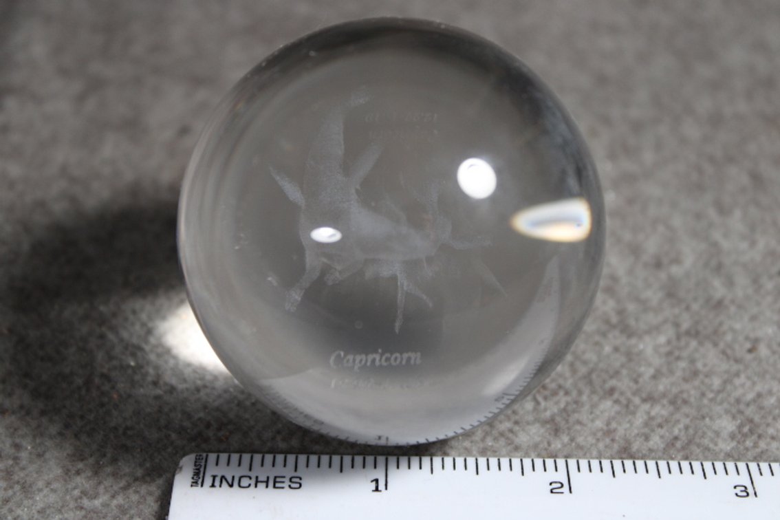 A glass sphere with the lasered image of the Zodiac sign Capricorn, sphere shown on a light box which is not included