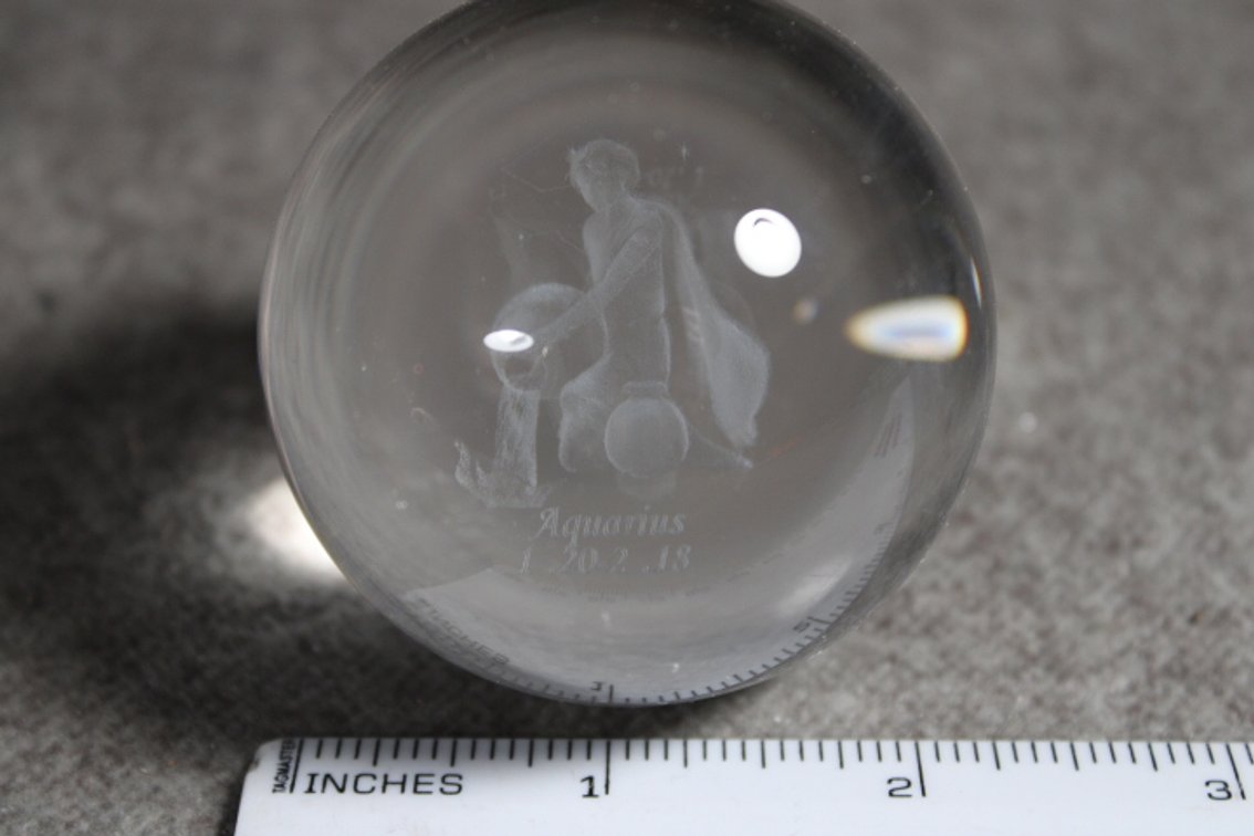 A glass sphere with the lasered image of the Zodiac sign Aquarius, sphere shown on light box which is not included