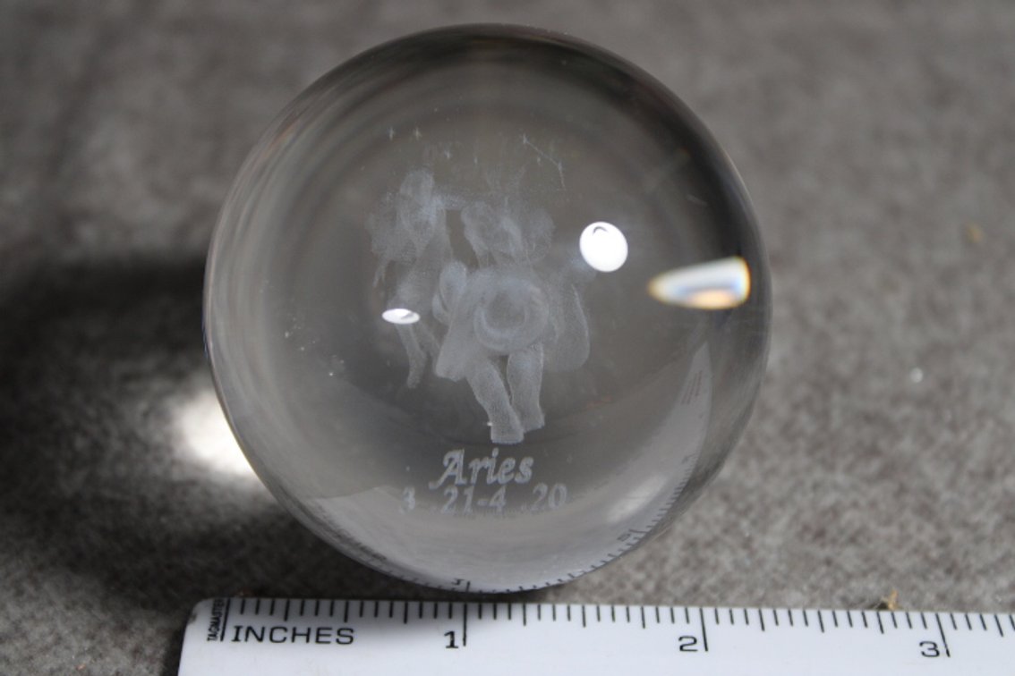 A glass sphere with the lasered image of the Zodiac sign Aries, sphere shown on a light box which is not included