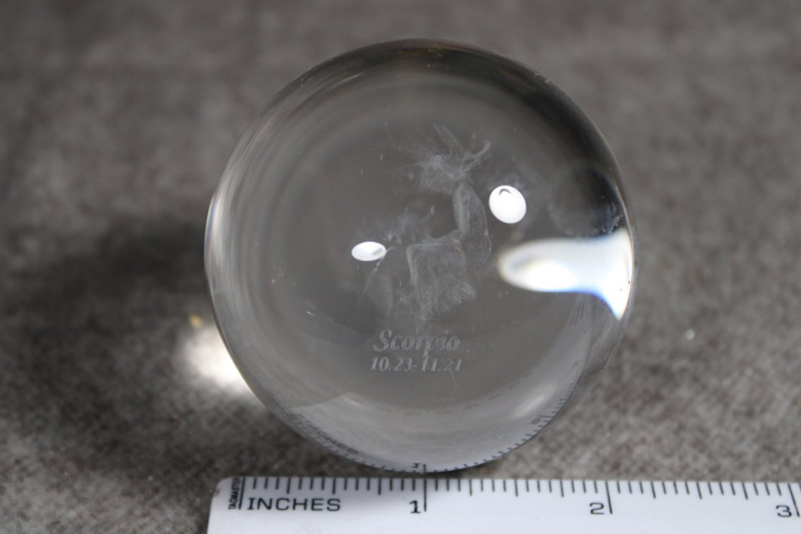 A glass sphere with the lasered image of the Zodiac sign Scorpio, sphere is shown on a light box which is not included