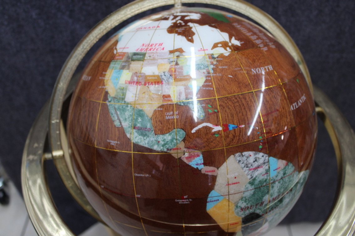 A floor standing globe and compass, with countries highlighted by inlay using different stones. The brass stand showing wear