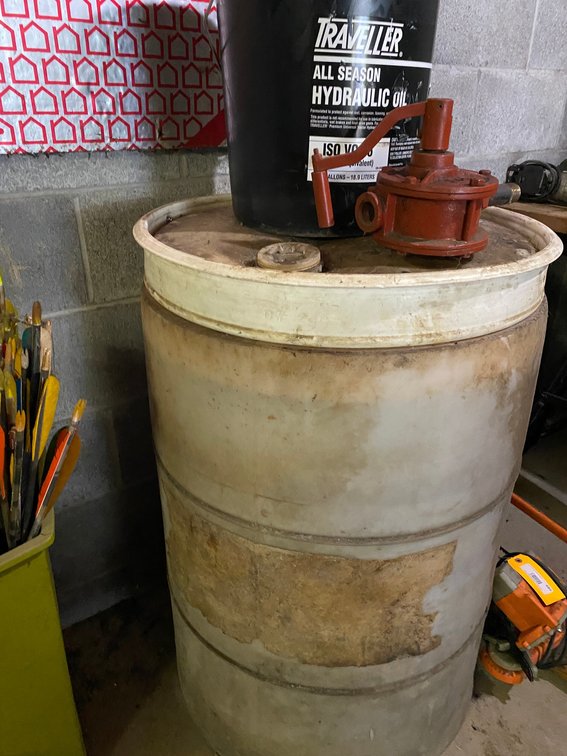 Drum mostly full of unknown content, 5-gal. bucket of hydraulic fluid and pump