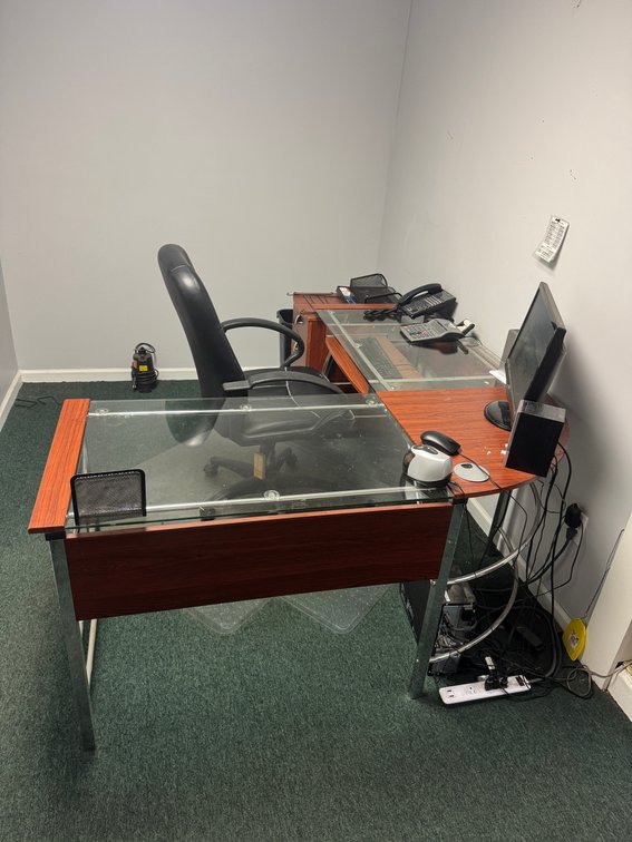 Glass-top office desk with wood-grain front panel and chrome-finish frame.