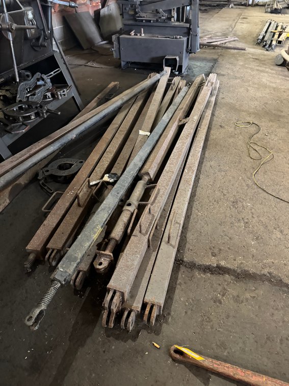 Assorted heavy-duty steel bars, linkage arms, and fabricated metal components in various lengths.