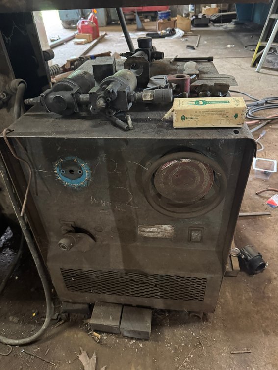 Older industrial welding/power unit with adjustable controls and assorted fittings/components stored on top.