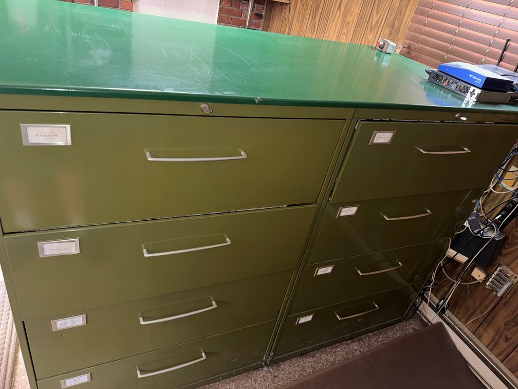 Two green metal lateral filing cabinets with multiple drawers, label holders, and locking tops.