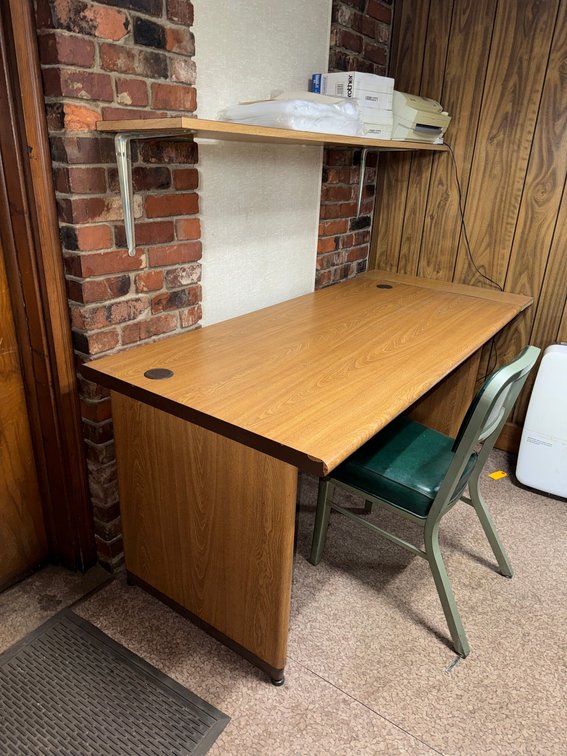Wood-grain office desk/workstation with overhead shelf and metal chair.