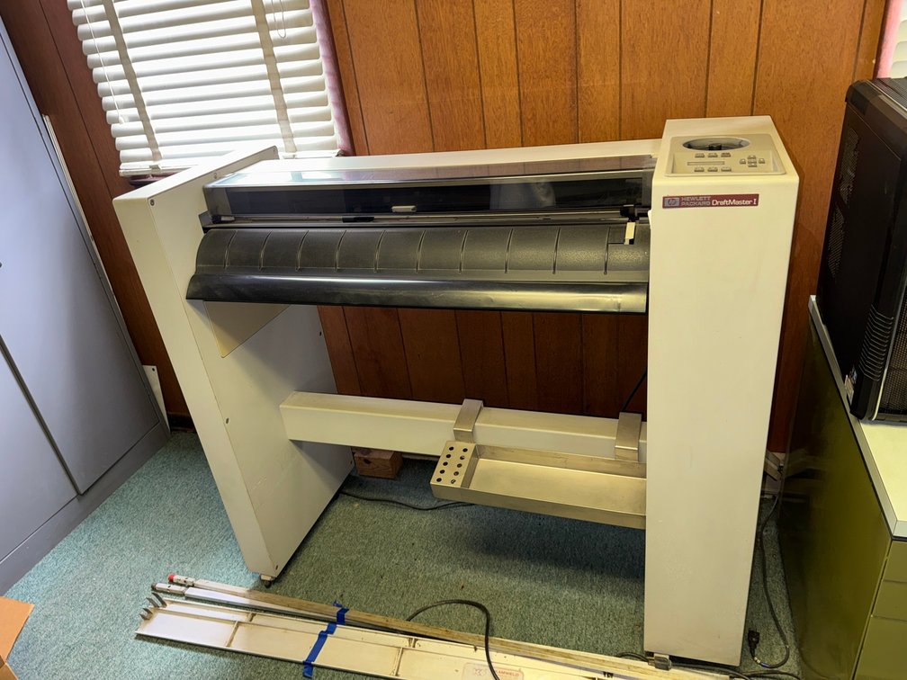 HP DesignJet large-format plotter/printer with stand and media roll support.