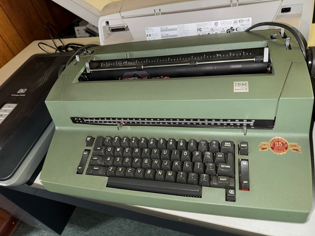Vintage IBM Selectric-style electric typewriter with full keyboard and heavy-duty metal housing.