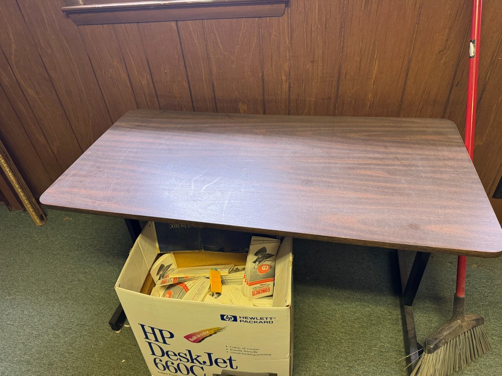 Wood-grain office/conference table with black metal legs and rectangular work surface.
