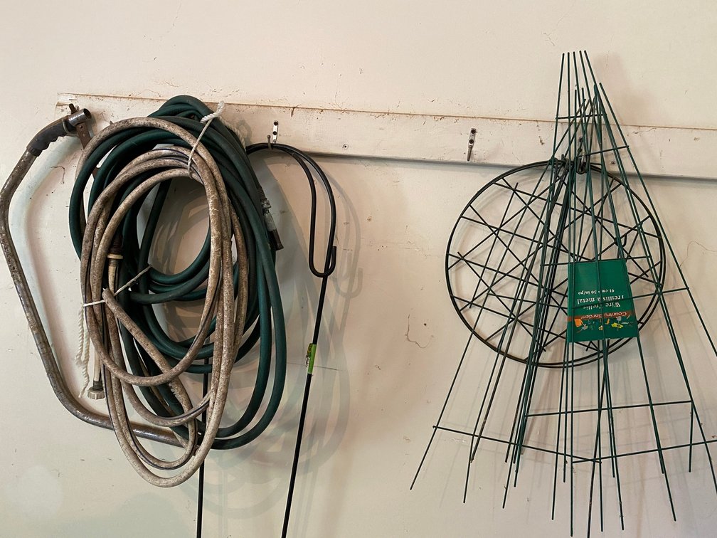 Shepherd's hook, garden hoses, bow saw, wire, trellis