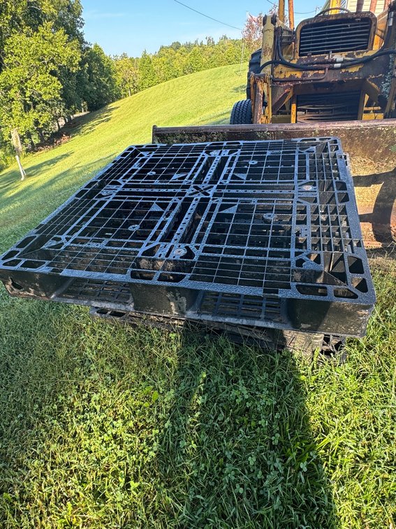 Stack of Used Black Molded Plastic Red Pallets Resting in the Grass