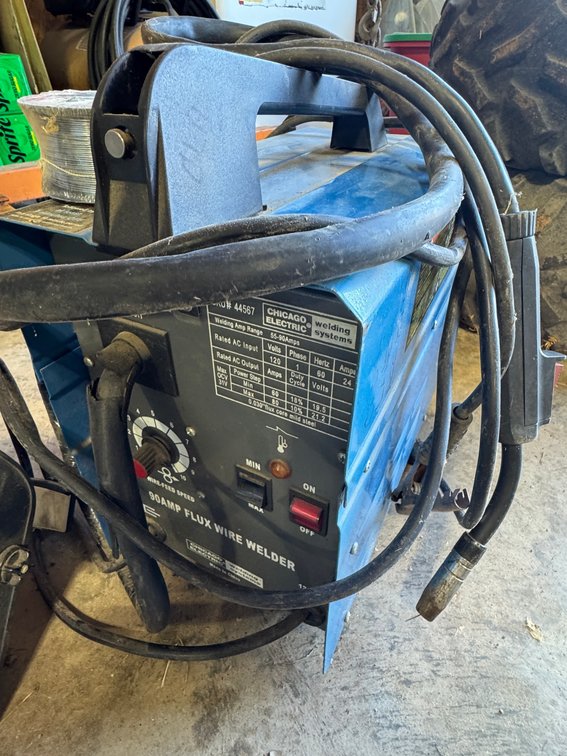 Blue chicago Electric 90 amp Flex Wire Welder with a Coil Power cord, Welding Mask and a Small Spool ofWire Resting on top