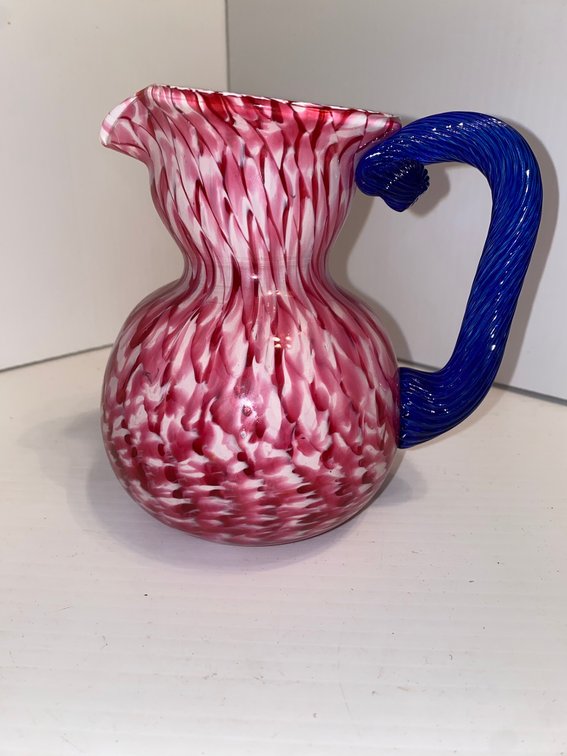 Vintage art glass pitcher featuring cranberry and white spatter with applied blue glass handle