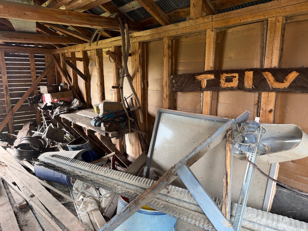 Contents of Wall and Floor with Bench Vise, Wheel Rims, Scythes, Sign, and More
