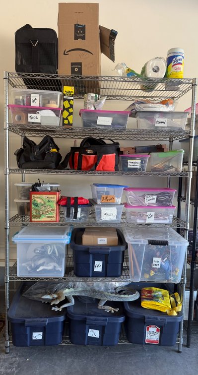 Metal shelving unit with contents including various tools, cords, decorations, tape, etc