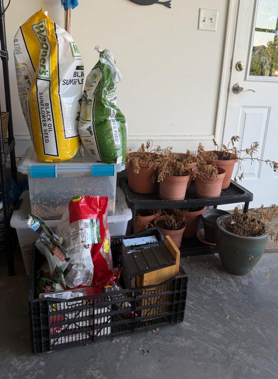 Multiple bags of birdseed, containers of birdseed, bird houses, collection of plant pots, etc