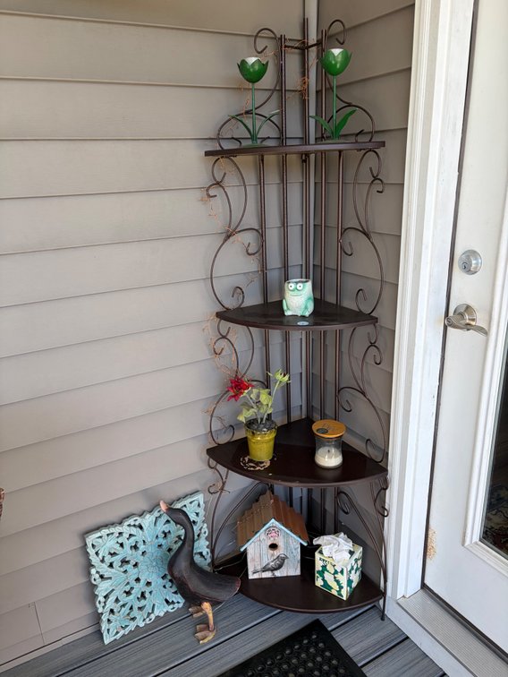 Outdoor 4 corner shelf unit with candle holders, birdhouse, wooden duck, miscellaneous decor pieces, and large rubber mat