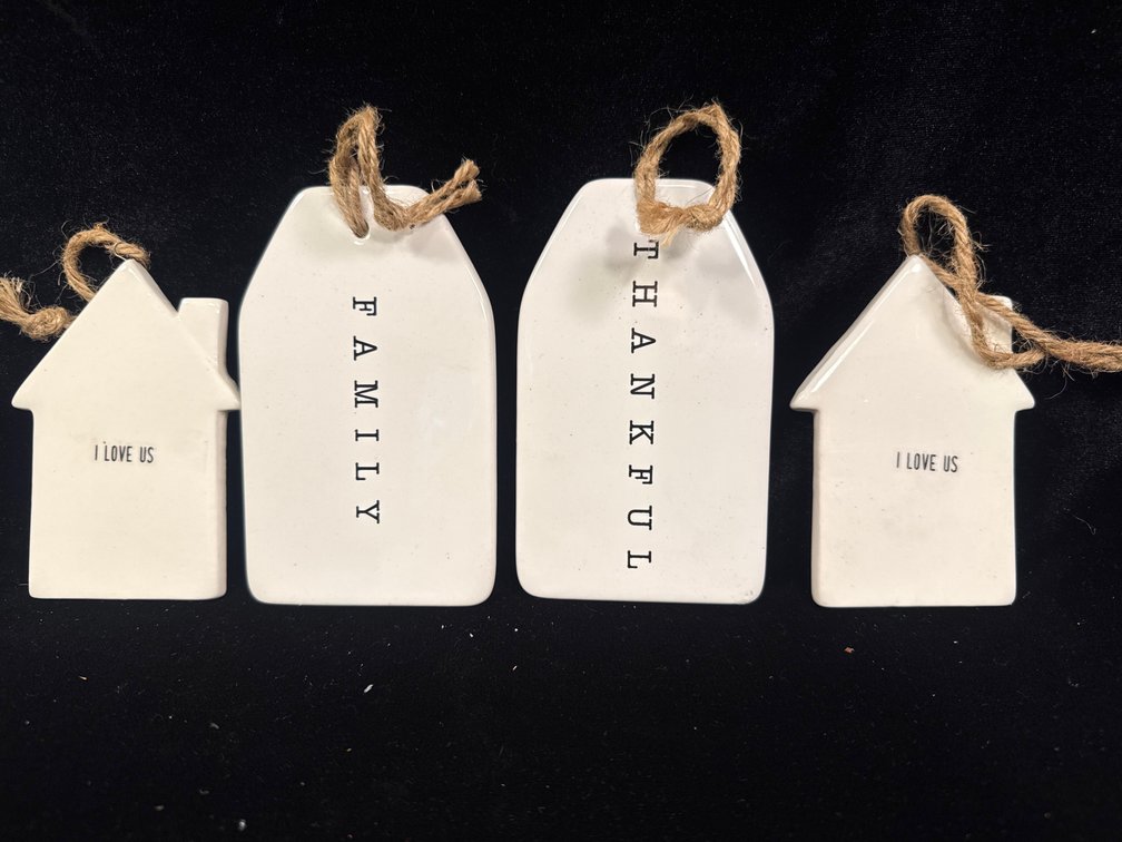set of white, house-shaped ceramic or clay hanging tags and ornaments strung with rustic twine, featuring embossed words like "I Love Us", "Family", and "Thankful"