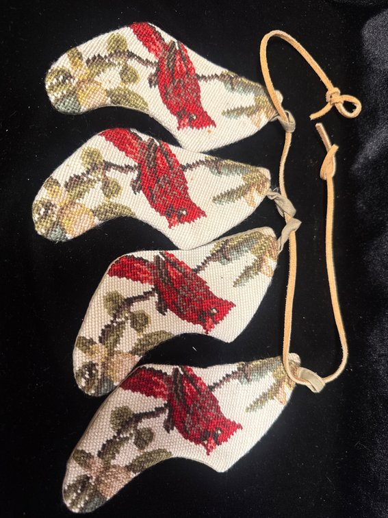 four handmade needlepoint or cross-stitch ornaments featuring a red cardinal perched on a branch, strung together with a leather cord