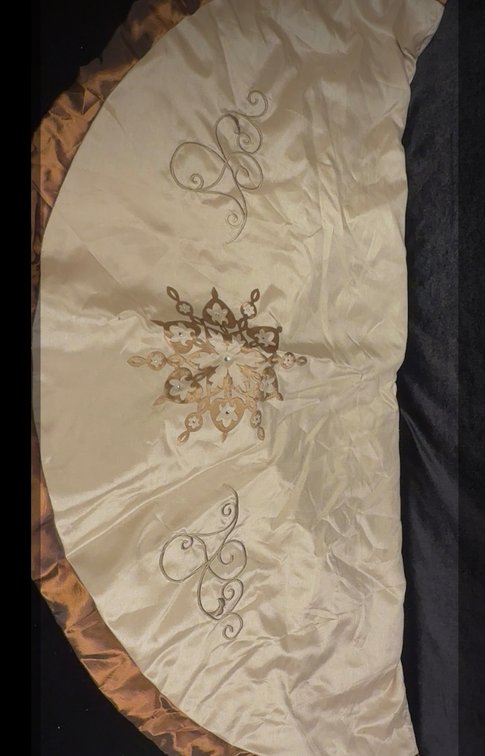 ivory and gold/tan embroidered Christmas tree skirt featuring a central floral or star medallion and decorative scrollwork/filigree motifs along the body and border