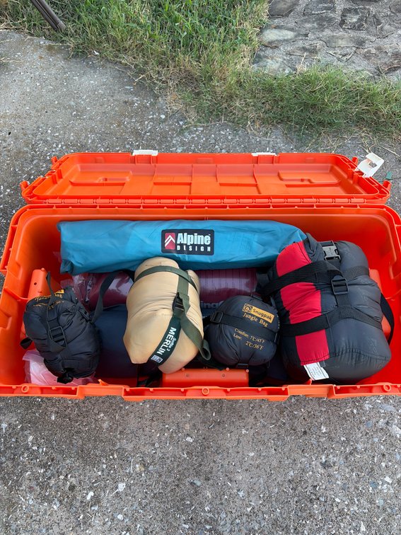 Camping gear in Orange Plano trunk, including tent, sleeping pads bags