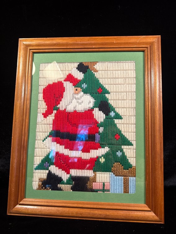 vintage Christmas-themed framed canvas needlepoint wall hanging depicting Santa Claus holding a Christmas tree and gifts