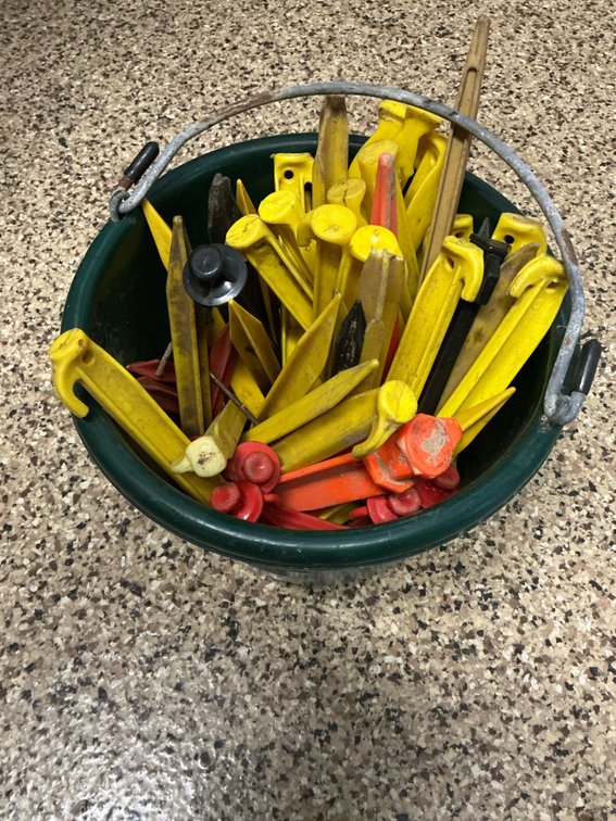 Assorted plastic tent stakes in green bucket