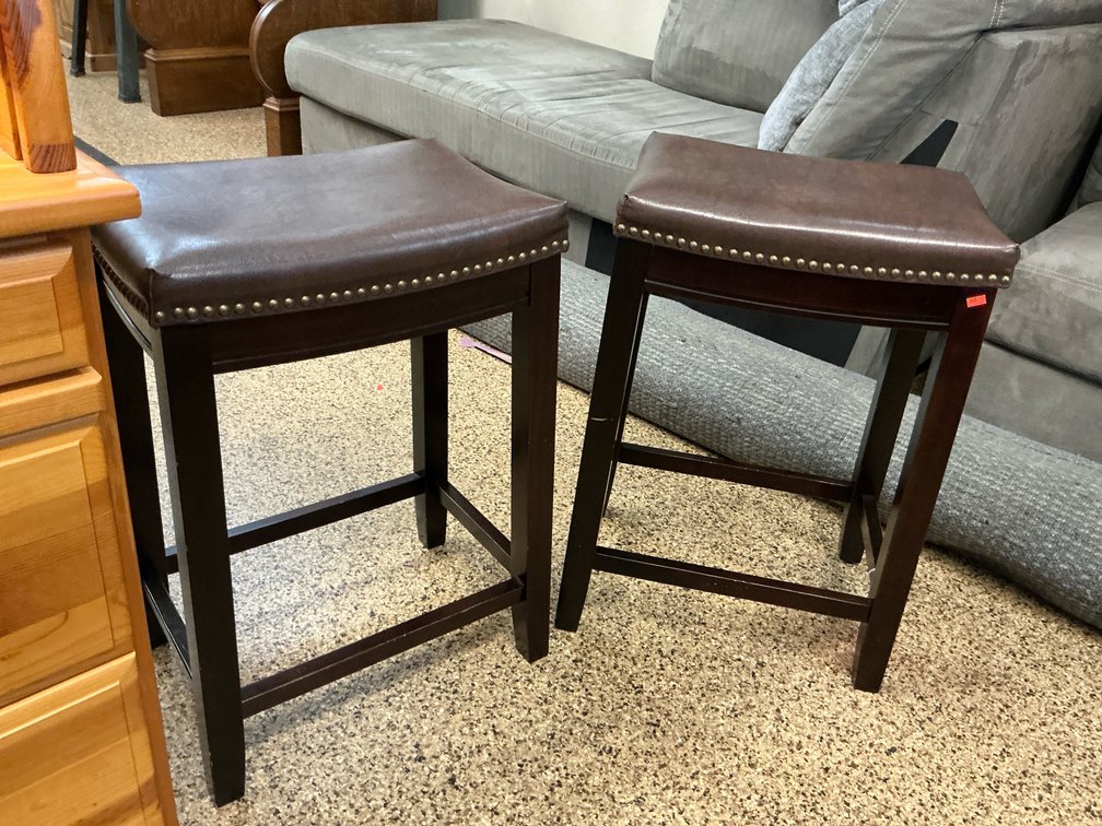 Pair of brown upholstered saddle stools with nailhead trim, 26” seat height