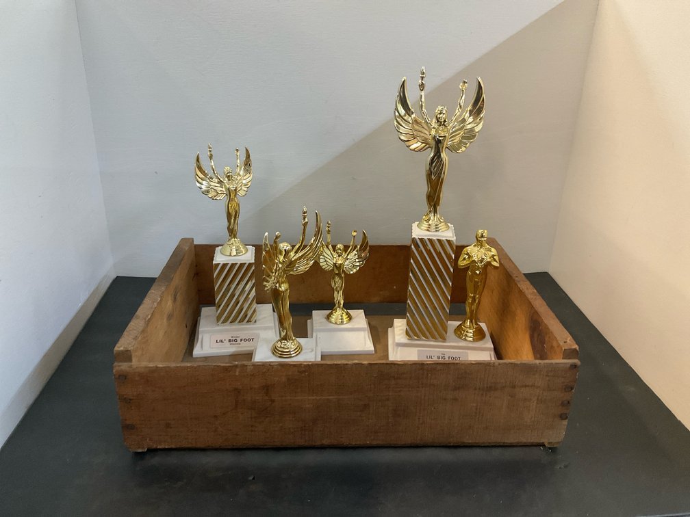 5 gold-tone Lil' Big Foot trophies in wooden crate