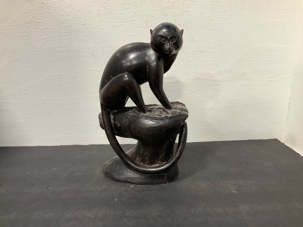 Carved dark wood seated monkey sculpture on pedestal