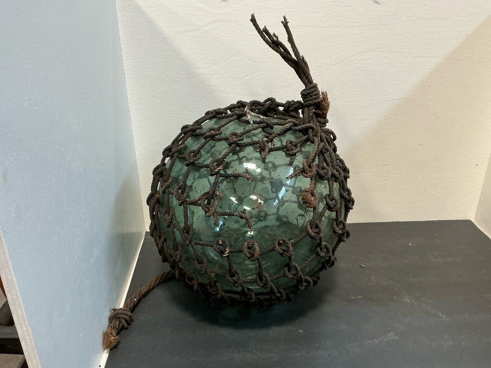 Green glass fishing float in knotted rope netting
