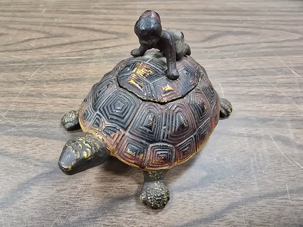 Cast iron turtle inkwell with black child on shelf.