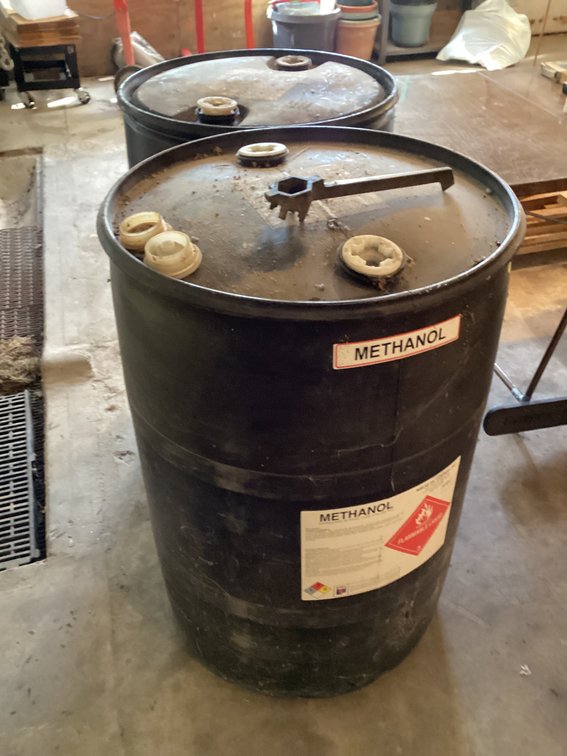 2 black plastic barrels. 1 has fluid in it