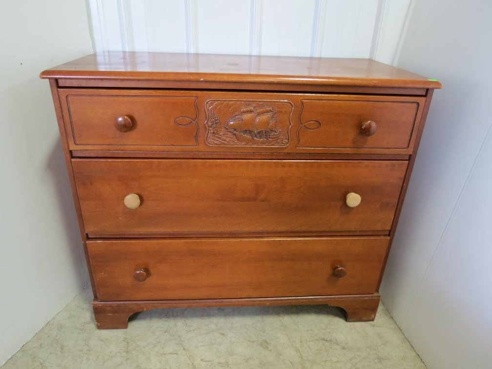 A three-drawer maple dresser by Emerson (New Hampshire) with a carved ship and castle on the top drawer.