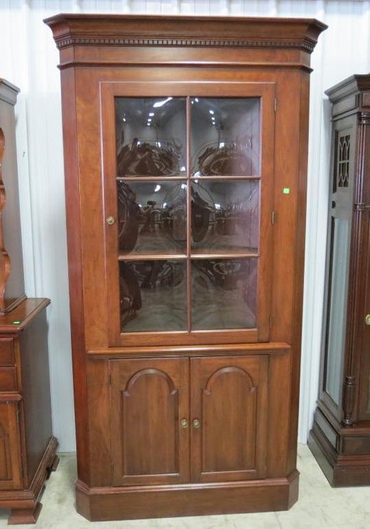 A cherry Pennsylvania House corner cabinet with glass door and two doors.
