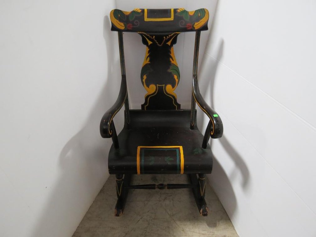 A wooden rocking chair with painted accents. Shows wear/damage in places.