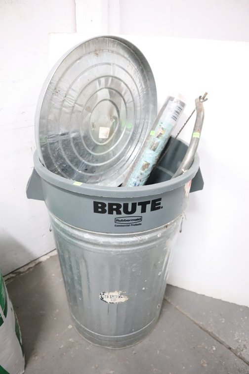 Metal and Rubbermaid Trash Can With Roll of Landscape Fabric and A Bow Saw
