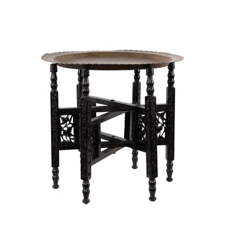 A brass-top table on a folding base intricately carved with foliage