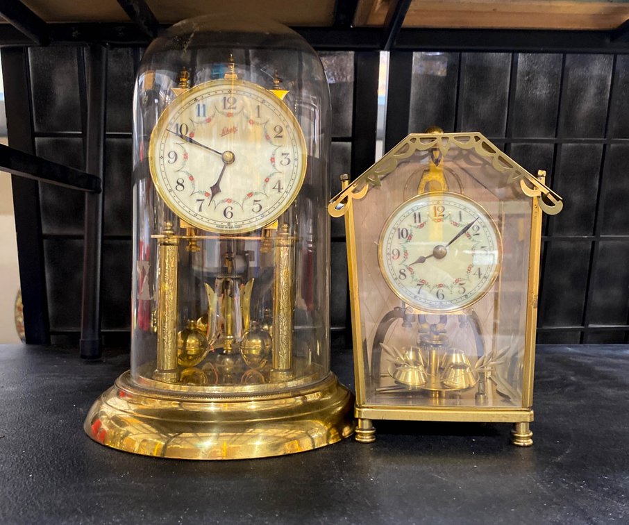 Two Brass Anniversary Clocks with Glass Domes and Pendulum Mechanisms