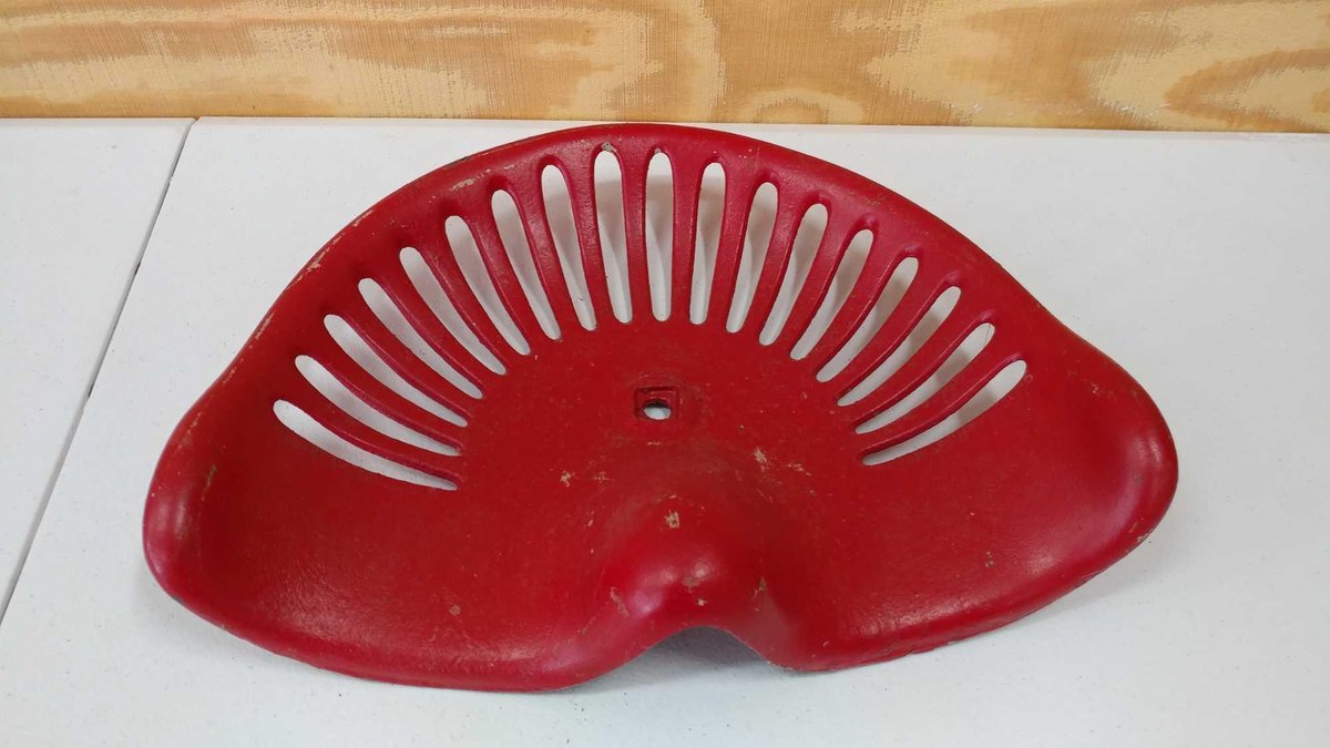 RED SEAT FOR A TRACTOR. IT HAS OBLONG HOLES.