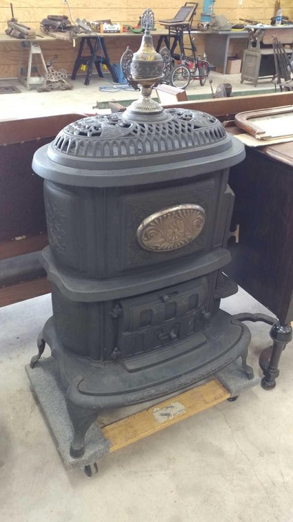 CAST IRON STOVE WAS USED TO HEAT A LIVING SPACE USING WOOD OR COAL. THE UPPER OVAL TOP HAS TWO LIDS 