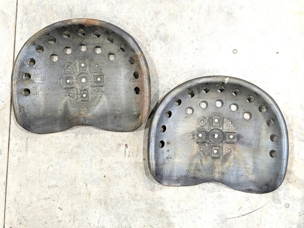 Two matching stamped steel tractor seats are each 18" wide.