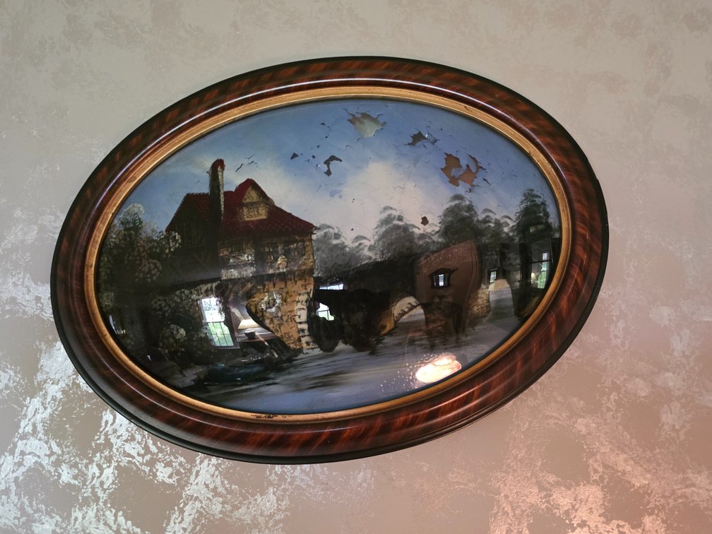 Reverse Painting on Convex Bubble Glass Featuring a scenic cottage or homestead landscape inside an oval wooden frame.