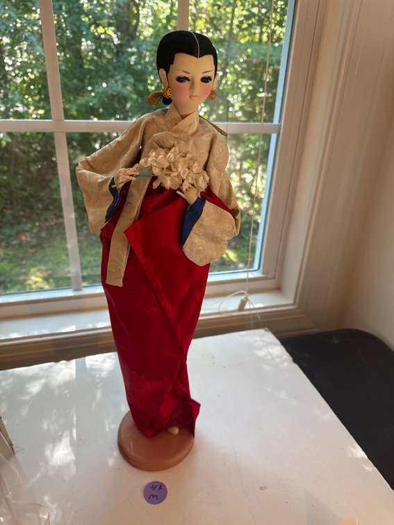 Vintage decorative doll wearing a traditional white and red silk hanbok-style outfit, holding a small floral accessory.