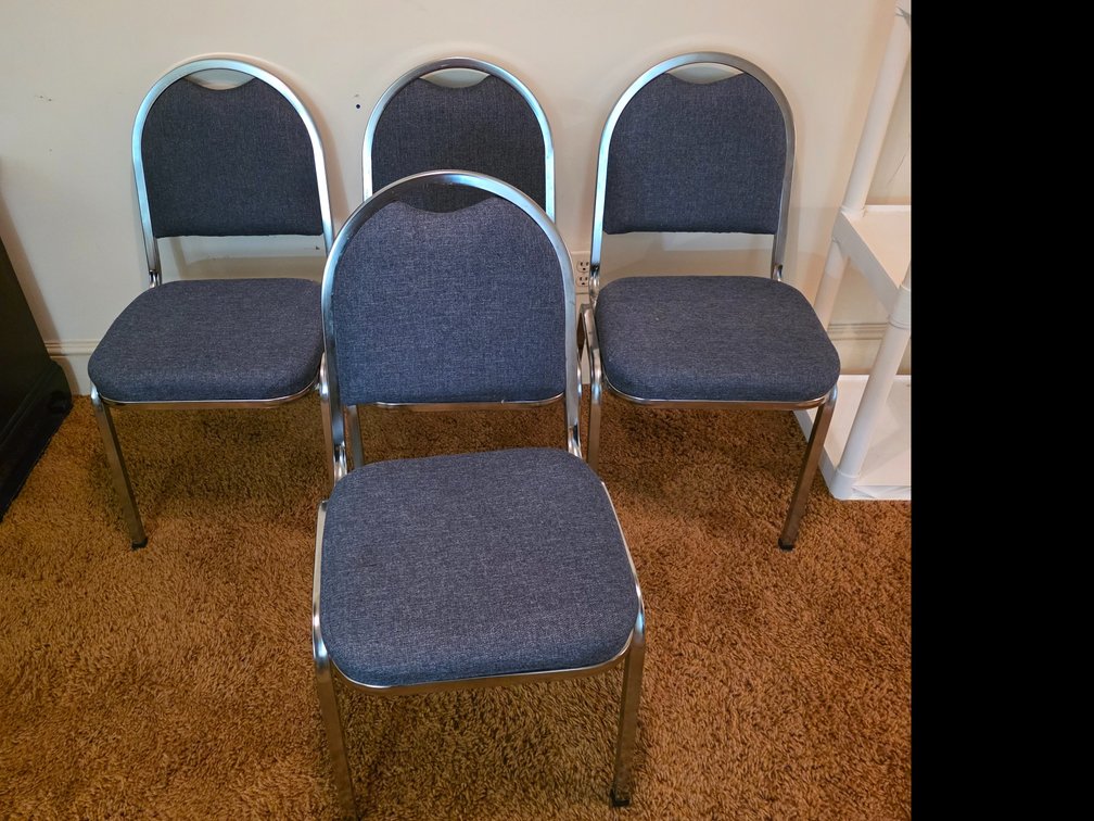 Blue fabric upholstered stacking banquet chair featuring a chrome metal frame and an arched handle cutout at the top of the backrest.