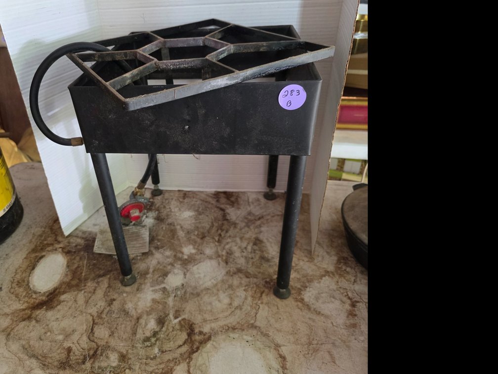 Black metal single-burner outdoor propane stove with a square cast-iron top grate and a hose with an adjustable regulator.